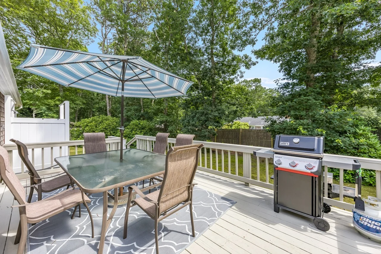 The spacious deck with a dining table, umbrella, and gas grill